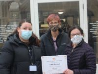 Lottie posing for a photo with people. They are all wearing masks and one is holding up a certificate.