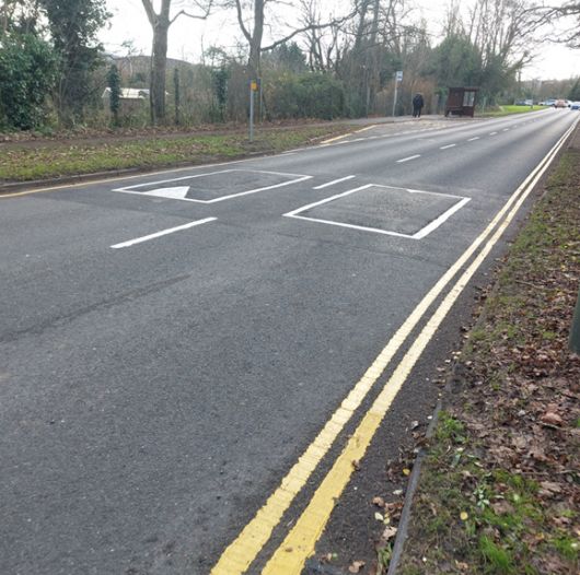 A road with newly painted double yellow lines and speed bumps