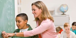 Teacher helps a child writing on a whiteboard