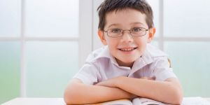 Young schoolboy smiles at camera, arms folded over a workbook