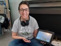 Young person smiling at the camera showing a tablet