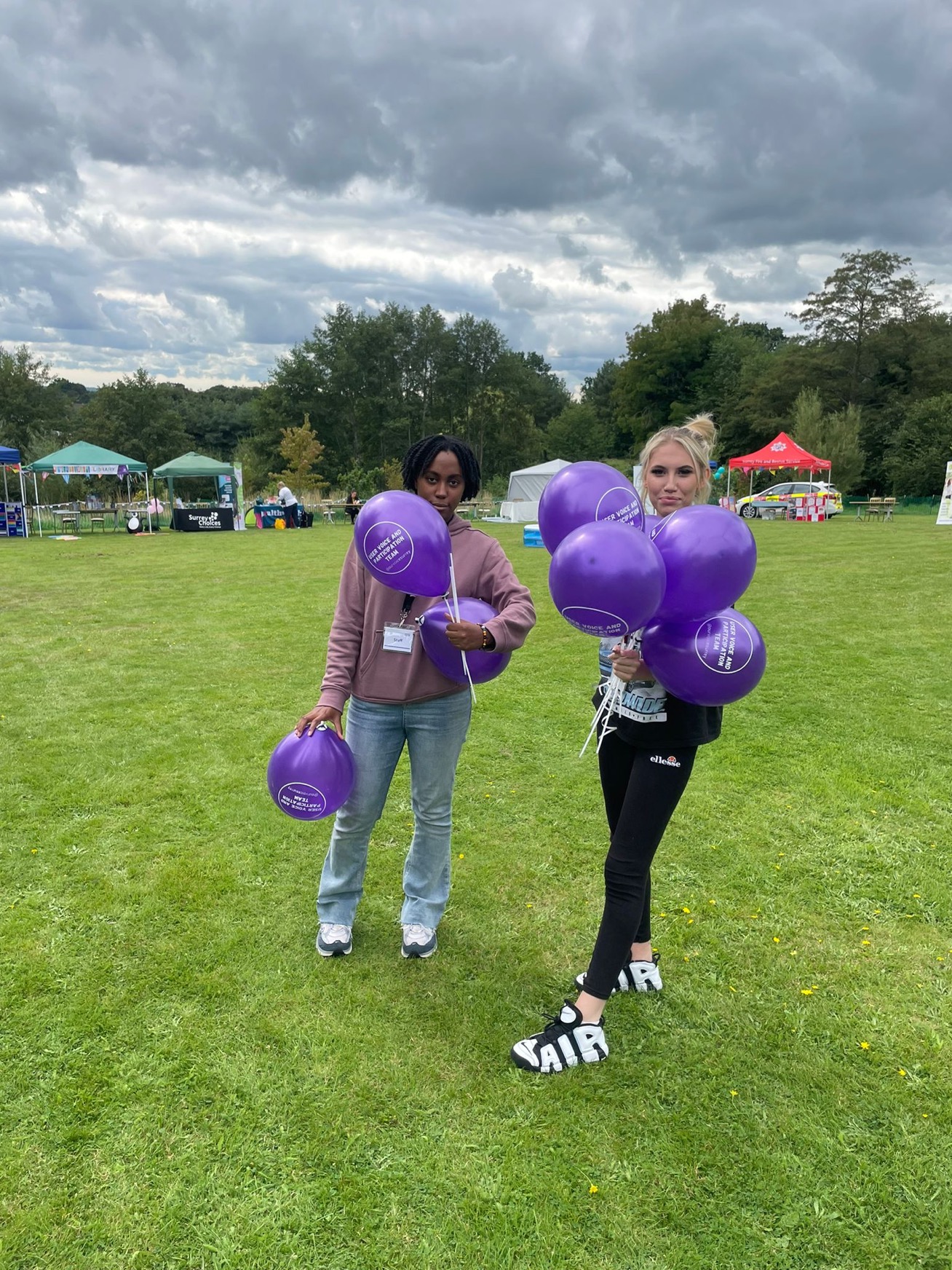 Two young woman in a field holding balloons.