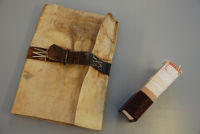 A 16c limp vellum binding and a mock up book featuring the possible different materials in its construction. From the bottom up there is a covering of goats skin leather then kraft paper and next is mull. The sewing is around cotton tape which is laced into pulp boards. At the head is a hand-sewn headband of two silk colours.