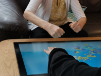 2 people looking at a sensory touch pad, one is touching the screen