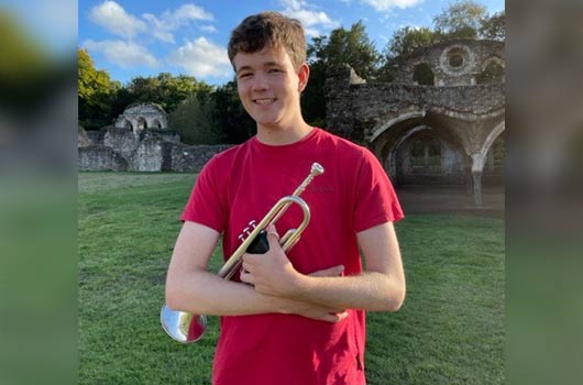 Ed Hinchliff smiling outside on a sunny day holding his brass trumpet