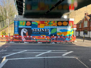Complete mural on the north wall of Staines Iron Bridge. The mural is brightly coloured and shows a swan, Staines bridge, Roman coins and Staines hop industry.