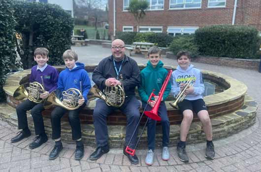 Four pupils and their tutor sitting together outside holding an assortment of brass instruments
