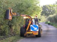 A tractor, with a hedge cutting attachment, cutting a roadside hedge