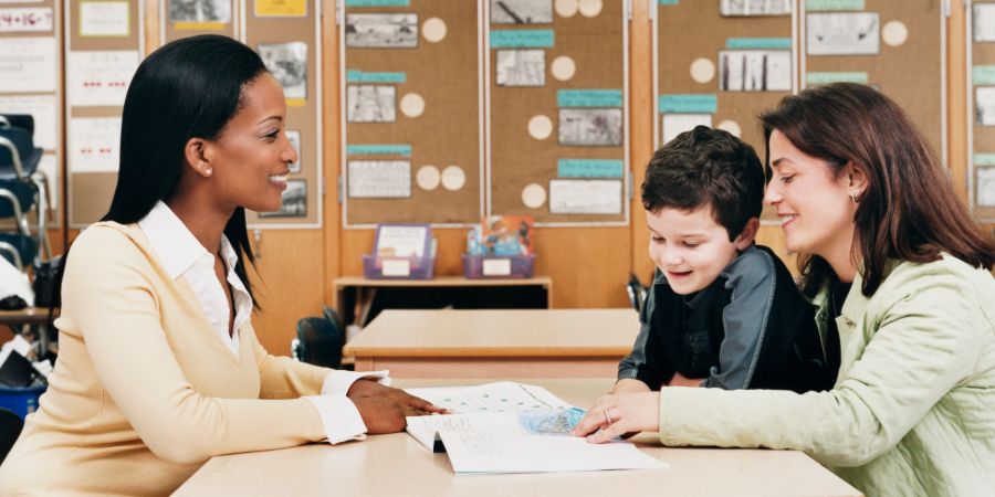 Mother and son discuss something with a teacher, over a table of paperwork