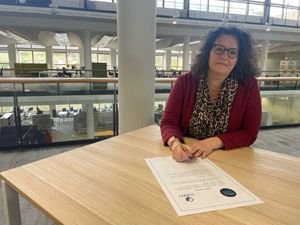 A woman sits at a table signing a document.