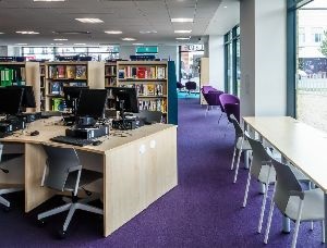 A library area with desks and chairs including computers and other desks for study and laptops