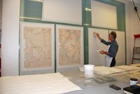 maps attached to a wall with a man working on them