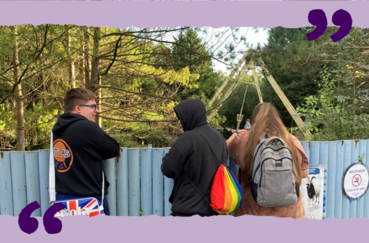 A group of three young people looking over a fence at a theme park ride.